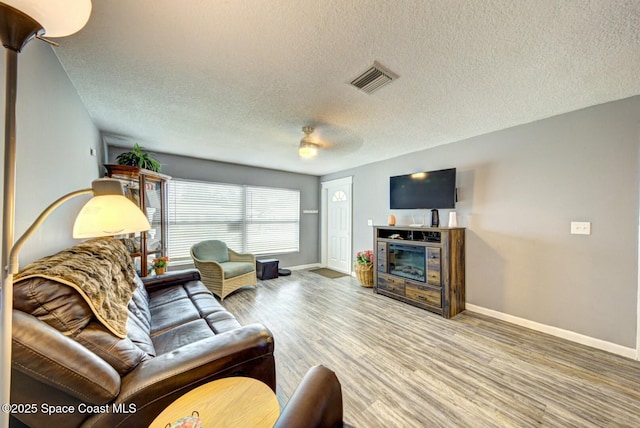 living area with a textured ceiling, wood finished floors, visible vents, and baseboards