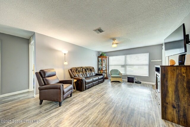 living area with visible vents, a textured ceiling, baseboards, and wood finished floors