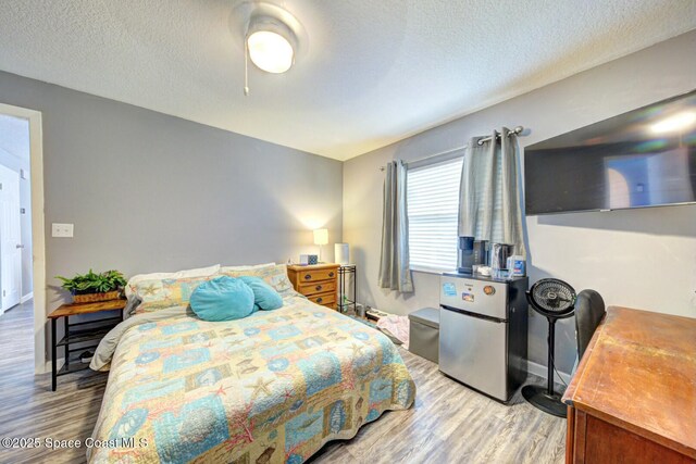 bedroom with baseboards, light wood finished floors, a textured ceiling, and freestanding refrigerator