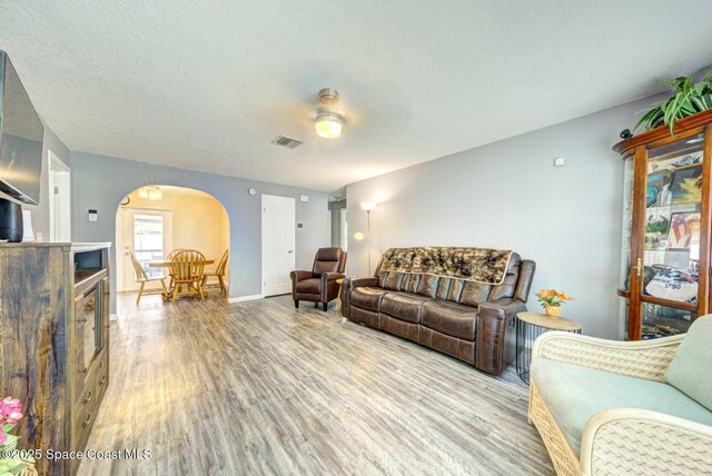 living area with visible vents, baseboards, wood finished floors, arched walkways, and a textured ceiling