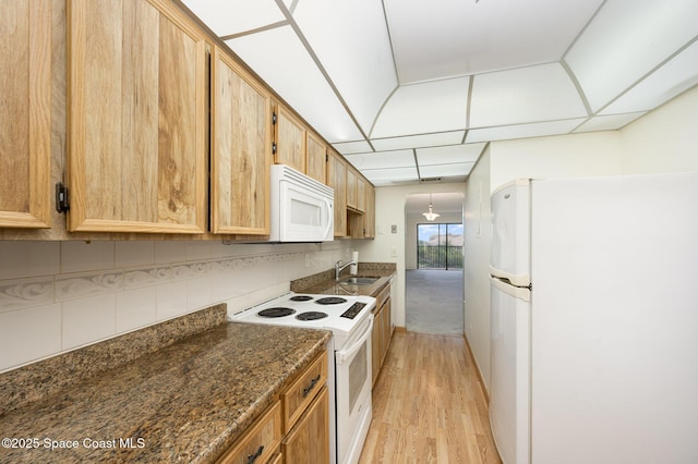 kitchen with decorative backsplash, white appliances, light wood-style floors, and a sink