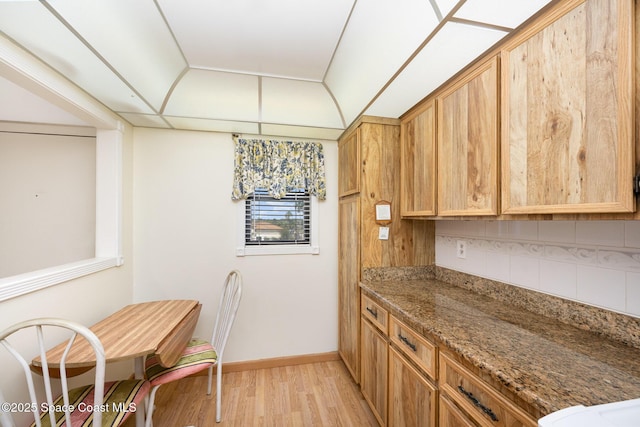 kitchen with stone counters, light wood-style flooring, baseboards, and backsplash