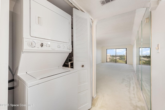 clothes washing area with visible vents, laundry area, stacked washer / drying machine, a textured ceiling, and light carpet