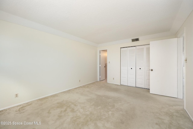 unfurnished bedroom with baseboards, visible vents, a closet, a textured ceiling, and light colored carpet