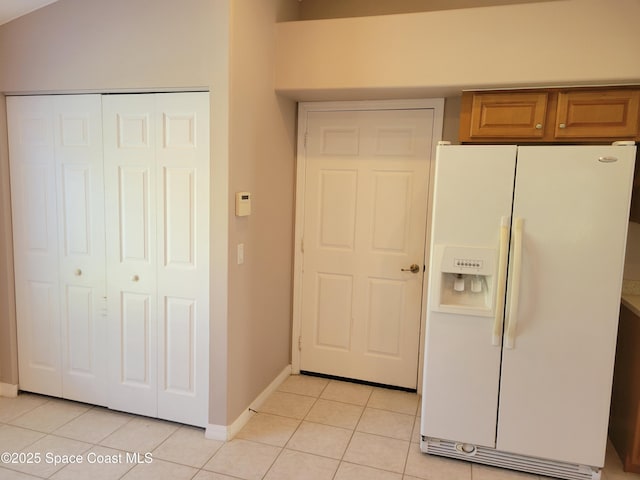 kitchen featuring brown cabinetry, baseboards, lofted ceiling, white fridge with ice dispenser, and light tile patterned flooring
