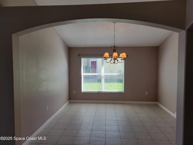 empty room with arched walkways, a chandelier, and baseboards