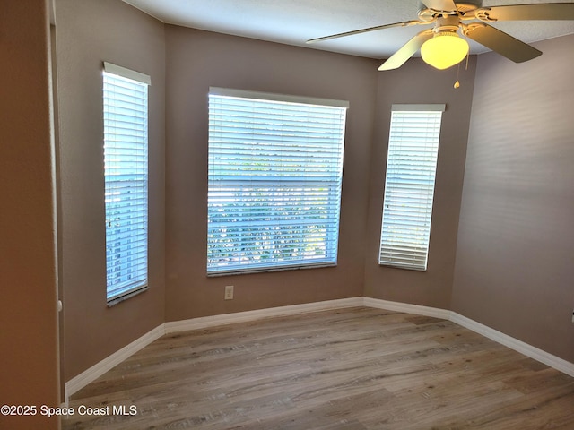 spare room featuring baseboards, light wood-type flooring, and ceiling fan