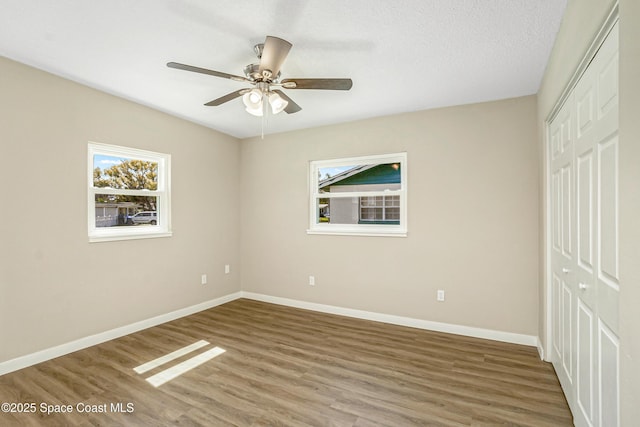 unfurnished bedroom featuring baseboards, a closet, wood finished floors, and ceiling fan