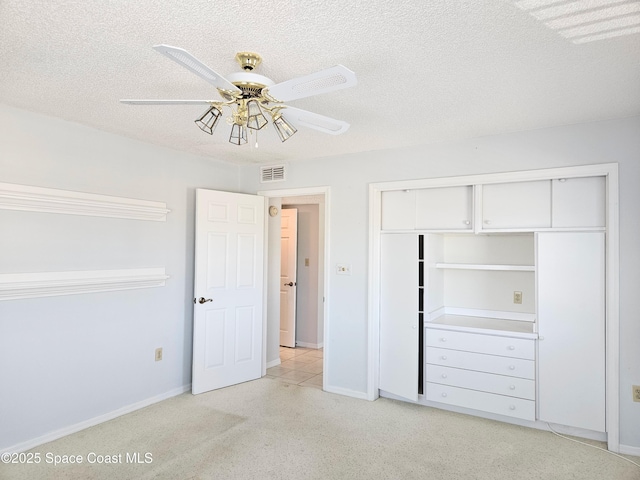 unfurnished bedroom with light colored carpet, a textured ceiling, ceiling fan, visible vents, and a closet
