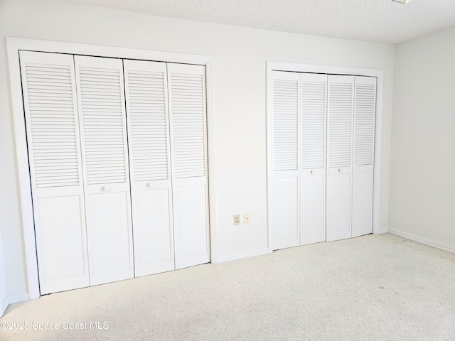 unfurnished bedroom featuring baseboards, carpet flooring, a textured ceiling, and multiple closets