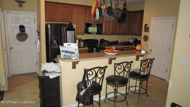 112 Broyles Dr SE, Palm Bay, FL 32909 - kitchen featuring light countertops, a kitchen breakfast bar, brown cabinetry, black appliances, and light tile patterned flooring