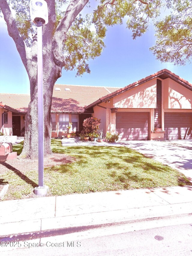 view of front of home with driveway, stucco siding, a front lawn, a garage, and a tiled roof