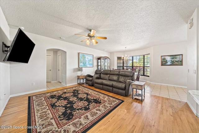 living room featuring a textured ceiling, light wood finished floors, baseboards, arched walkways, and ceiling fan with notable chandelier