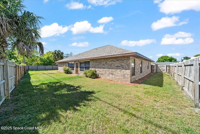 rear view of property featuring brick siding, a fenced backyard, and a yard