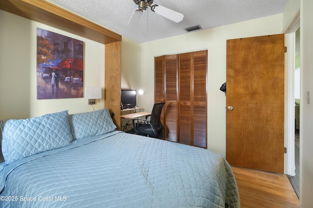 bedroom featuring a textured ceiling, visible vents, a ceiling fan, a closet, and wood finished floors