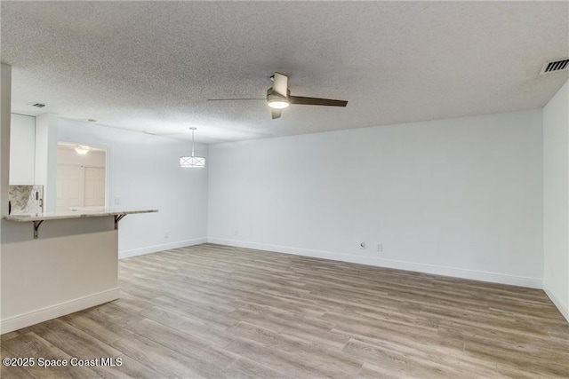 unfurnished living room featuring visible vents, baseboards, light wood-type flooring, a textured ceiling, and a ceiling fan