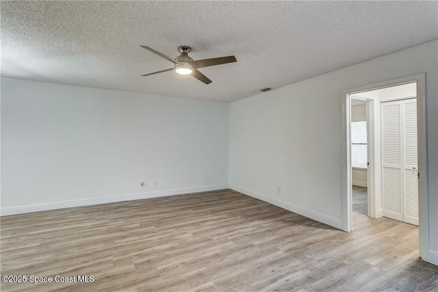 empty room with a textured ceiling, baseboards, light wood finished floors, and ceiling fan