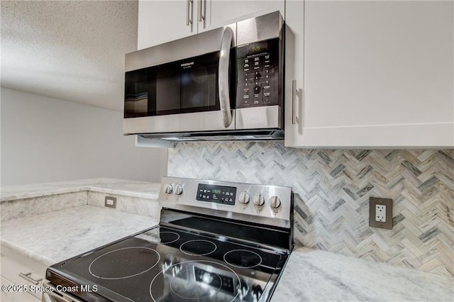 kitchen with backsplash, a textured ceiling, white cabinetry, appliances with stainless steel finishes, and light stone countertops