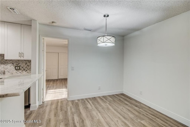unfurnished dining area with light wood-type flooring, baseboards, a textured ceiling, and visible vents