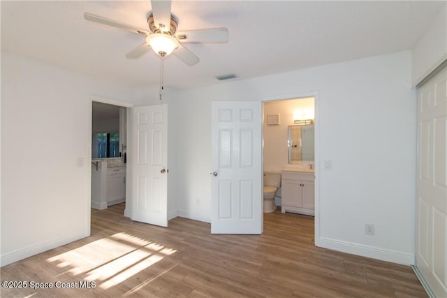 unfurnished bedroom featuring ensuite bath, wood finished floors, visible vents, and baseboards
