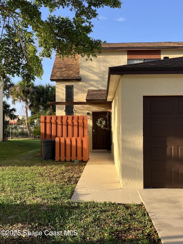 entrance to property with a garage, a shingled roof, stucco siding, and a yard