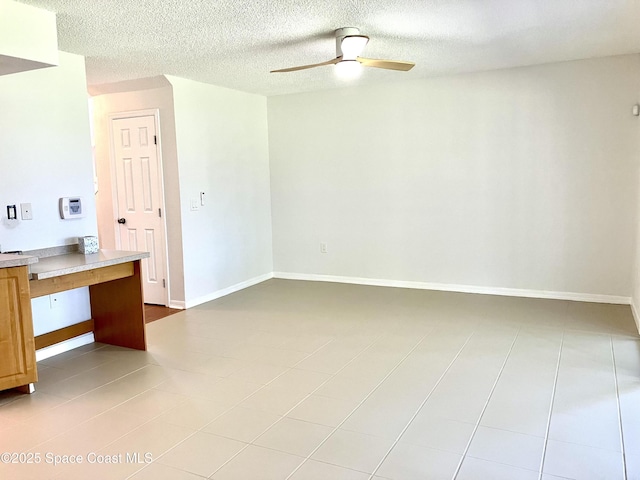 unfurnished room with a textured ceiling, ceiling fan, light tile patterned floors, and baseboards