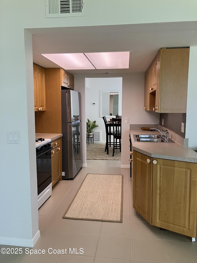 kitchen featuring freestanding refrigerator, gas stove, visible vents, a sink, and light tile patterned flooring