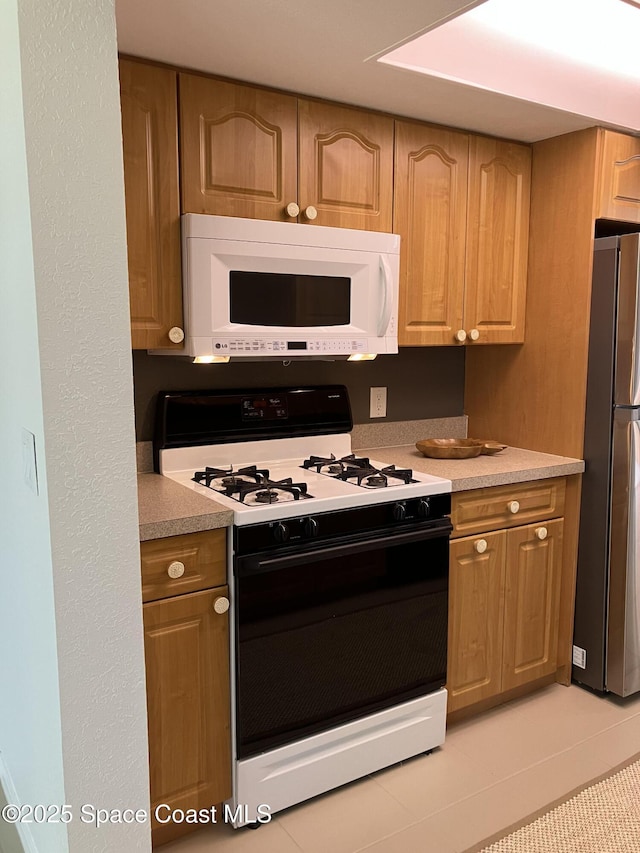 kitchen with light countertops, white microwave, range with gas stovetop, and freestanding refrigerator