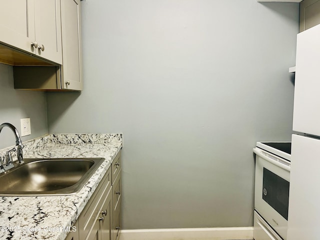 kitchen featuring white appliances, baseboards, and a sink