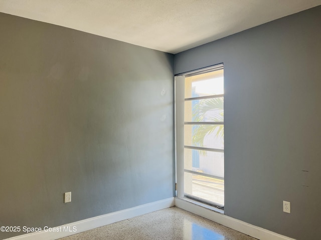 unfurnished room featuring speckled floor and baseboards