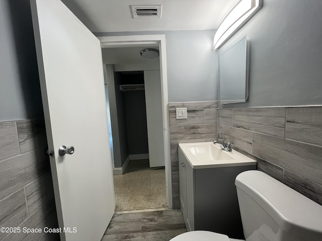 half bathroom with visible vents, a wainscoted wall, toilet, vanity, and tile walls