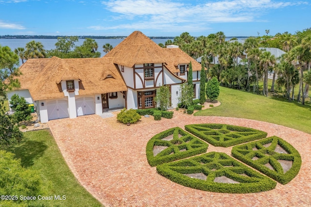 7021 S Tropical Trl, Merritt Island, FL 32952 - english style home with decorative driveway, stucco siding, a garage, a front lawn, and a water view