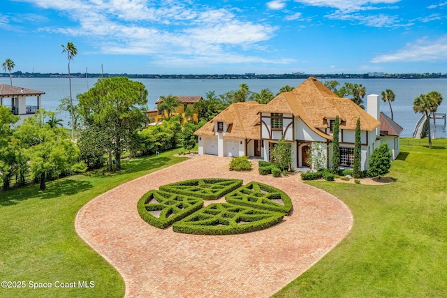 7021 S Tropical Trl, Merritt Island, FL 32952 - tudor home featuring curved driveway, stucco siding, a garage, a water view, and a front lawn