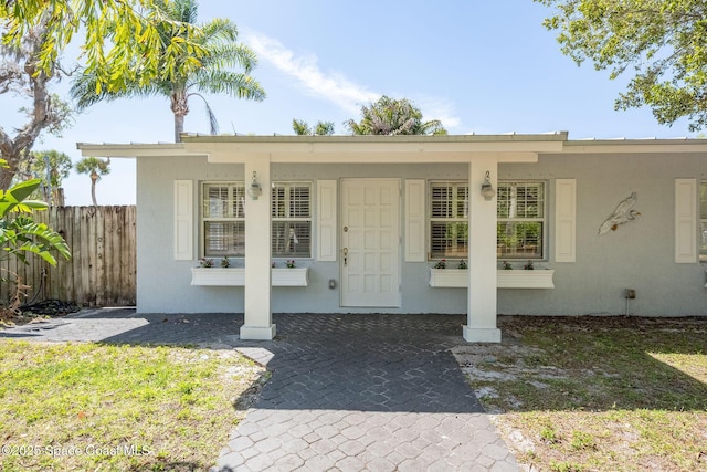 doorway to property featuring stucco siding and fence