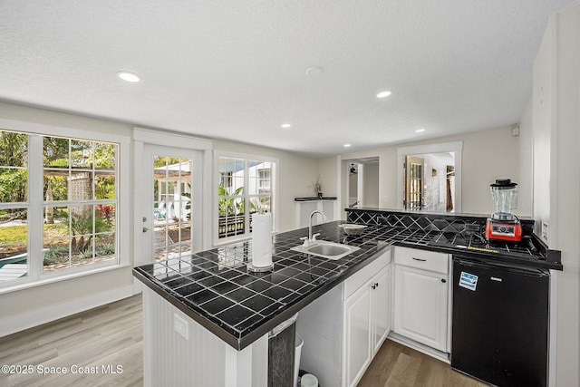 kitchen with dishwashing machine, tile counters, light wood finished floors, and a sink