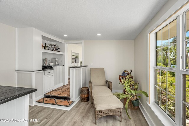 living area with recessed lighting, a textured ceiling, light wood-type flooring, and baseboards