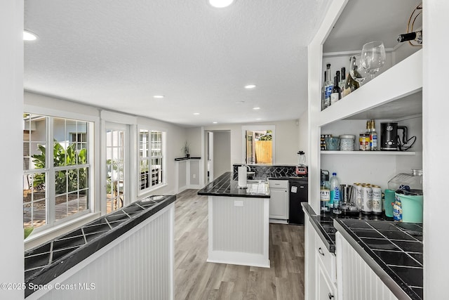 kitchen featuring a textured ceiling, dark countertops, white cabinetry, light wood finished floors, and dishwasher