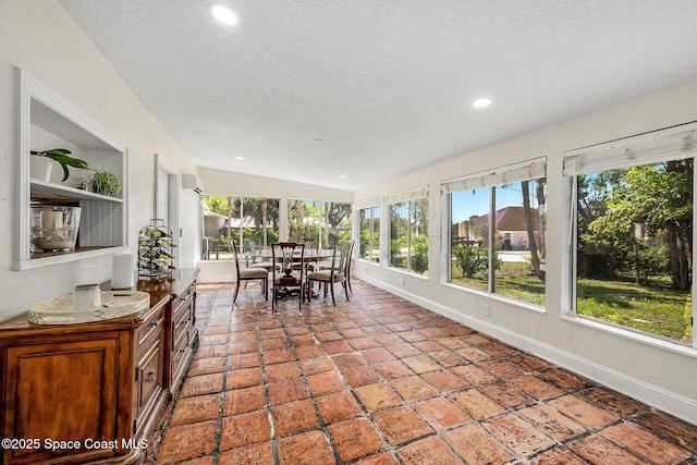 unfurnished sunroom featuring recessed lighting, baseboards, plenty of natural light, and a textured ceiling
