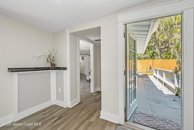 doorway to outside featuring wood finished floors, baseboards, and a textured ceiling