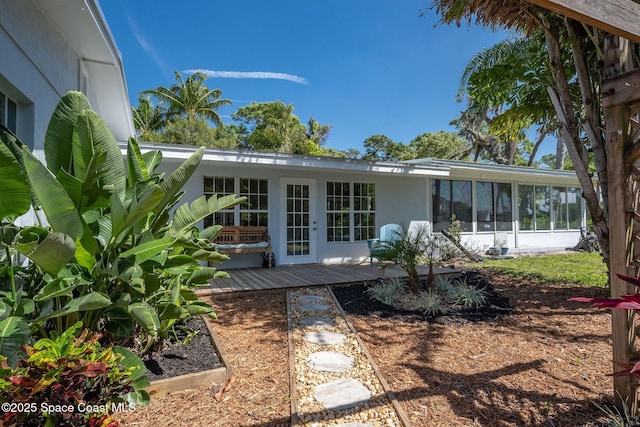 rear view of property featuring a deck, french doors, a sunroom, and stucco siding