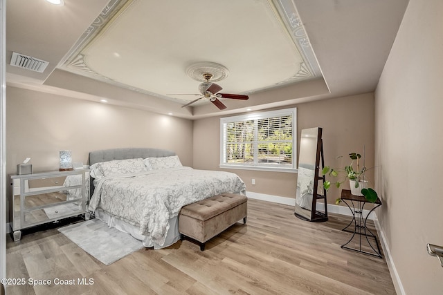 bedroom with visible vents, baseboards, light wood-type flooring, a tray ceiling, and a ceiling fan