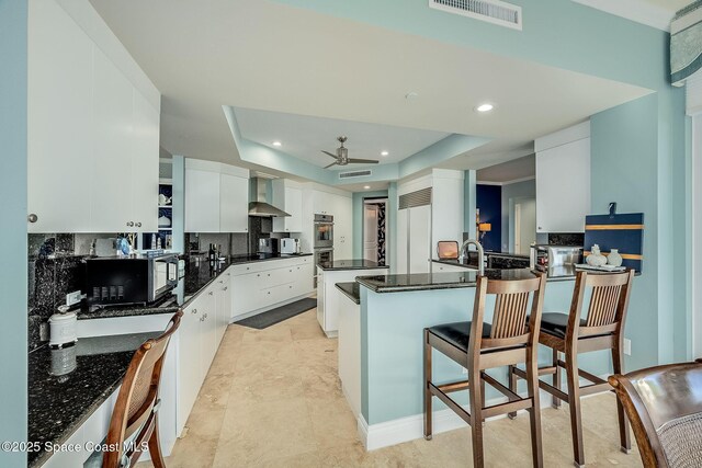 601 N Swim Club Dr Pha, Pha, Indian River Shores, FL 32963 - kitchen with visible vents, a raised ceiling, ceiling fan, wall chimney range hood, and a peninsula