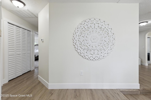 corridor featuring wood finished floors, arched walkways, and a textured ceiling
