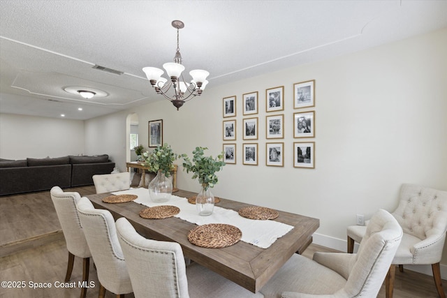 dining space with visible vents, wood finished floors, arched walkways, and an inviting chandelier