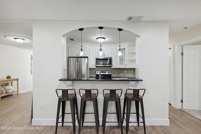 kitchen with white cabinets, visible vents, appliances with stainless steel finishes, arched walkways, and a breakfast bar area