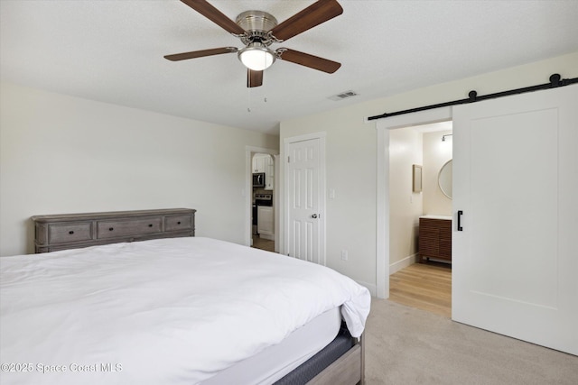 bedroom with ensuite bathroom, visible vents, a ceiling fan, light carpet, and a barn door