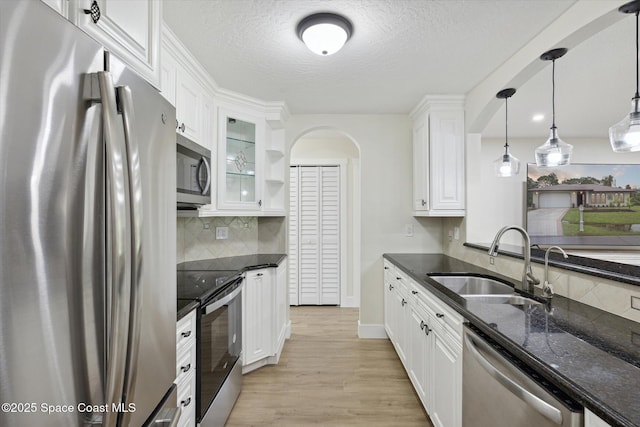 kitchen featuring white cabinetry, dark stone counters, a sink, light wood-style flooring, and appliances with stainless steel finishes