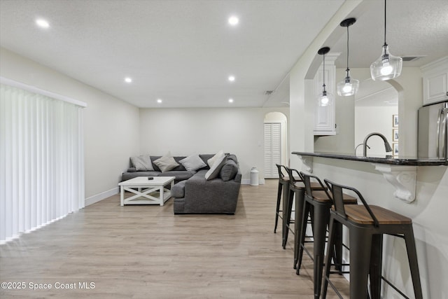living area featuring arched walkways, baseboards, recessed lighting, and light wood finished floors