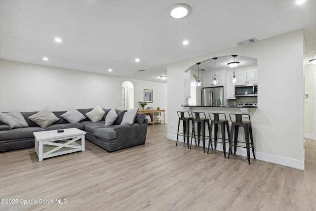 living area with visible vents, baseboards, recessed lighting, arched walkways, and light wood-style floors