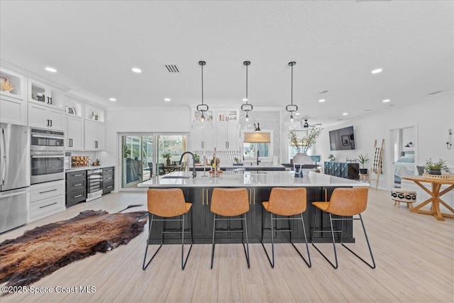 kitchen with a sink, freestanding refrigerator, a kitchen bar, visible vents, and white cabinets